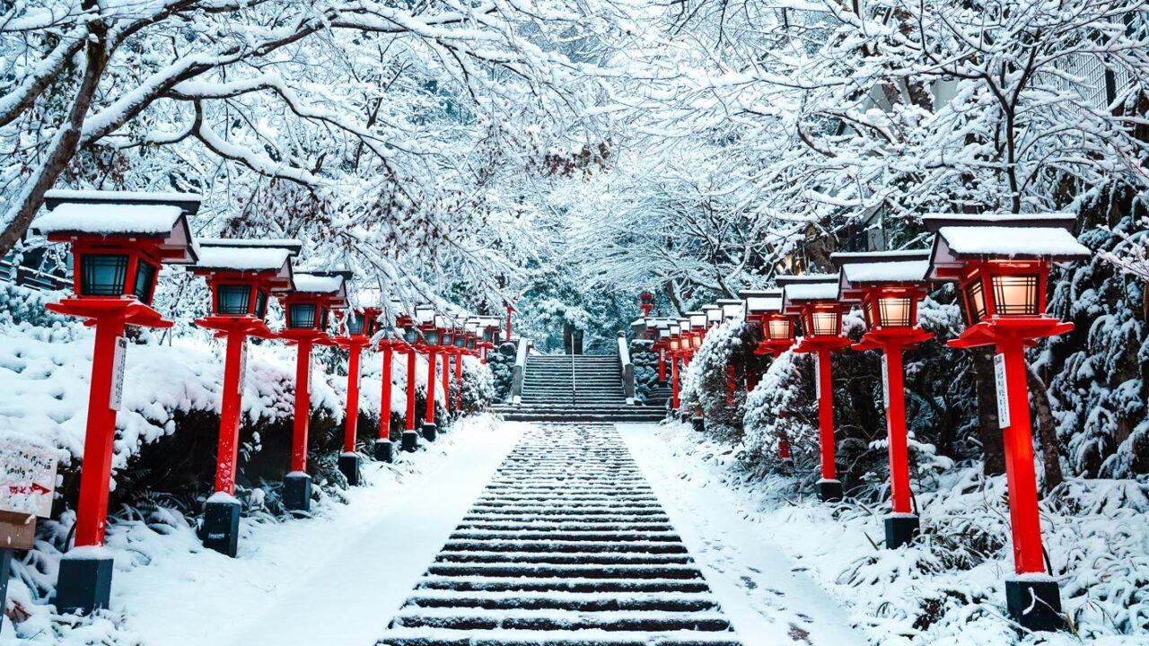 UnViaggioPerDue: Una passerella coperta di neve con lanterne rosse in Giappone durante la stagione invernale.