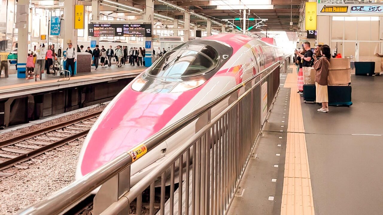 UnViaggioPerDue: Un treno ad alta velocità rosa e bianco, ispirato a Hello Kitty, in una stazione ferroviaria giapponese.