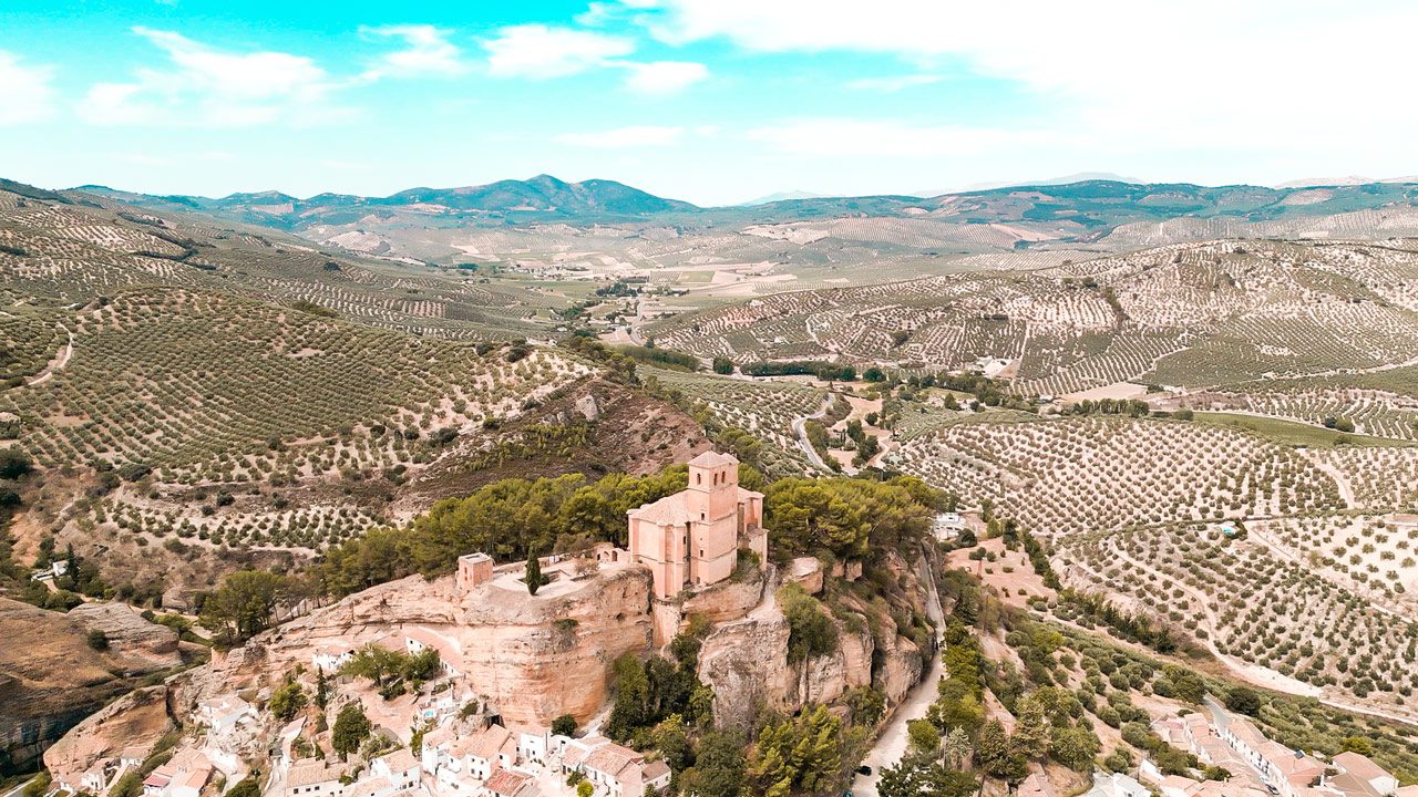 UnViaggioPerDue: Veduta aerea di uno storico castello arroccato su una scogliera sopra un vasto paesaggio punteggiato da filari di ulivi, circondato dalle dolci colline dell'Andalusia.