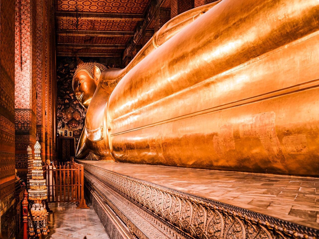 UnViaggioPerDue: Una grande statua dorata del Buddha sdraiato è esposta all'interno del tempio Wat Pho riccamente decorato, con intricati motivi sulle pareti e sulle colonne.