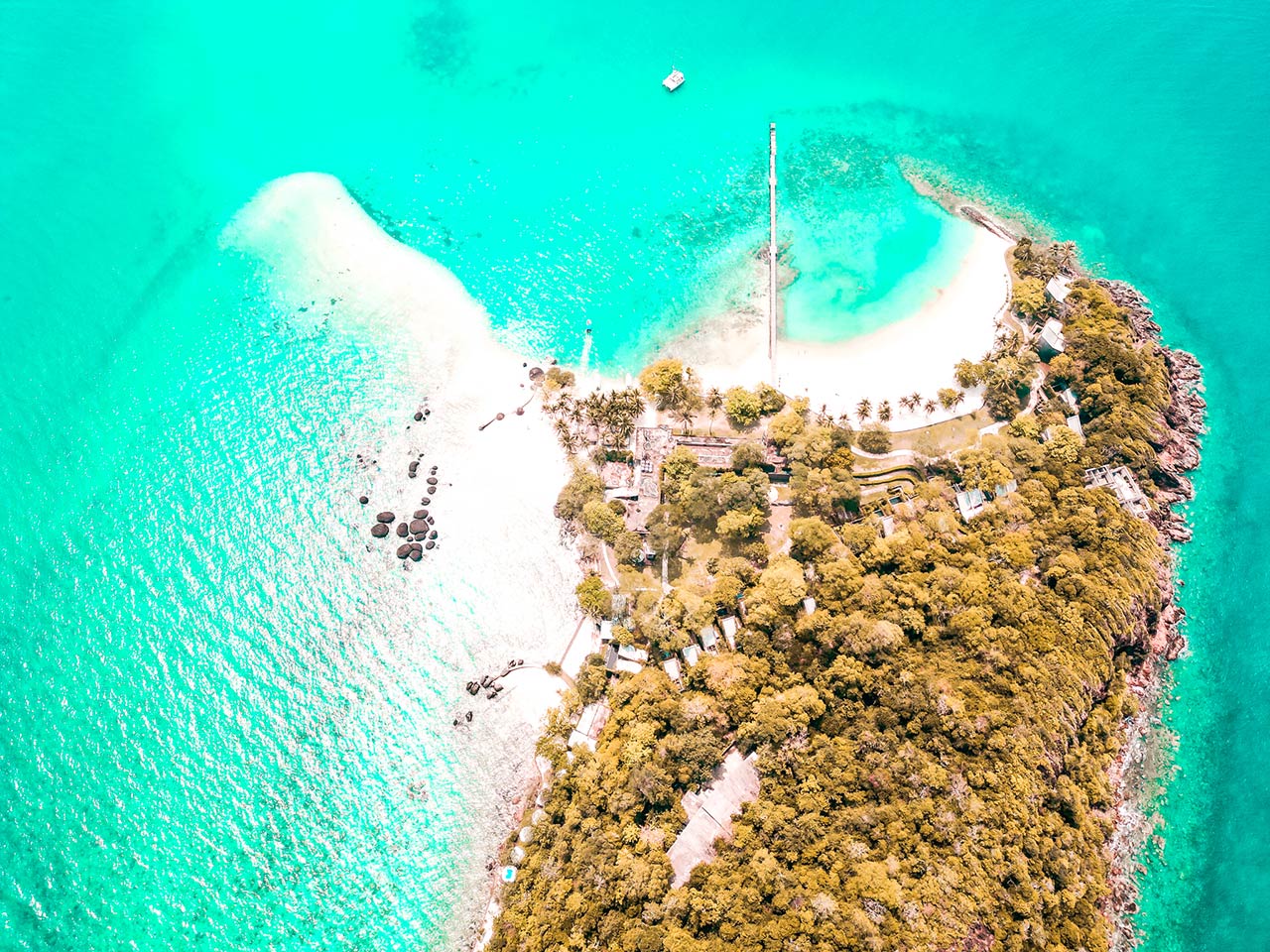 UnViaggioPerDue: vista aerea di una pittoresca isola tropicale, Koh Kham, con acque turchesi limpide, spiagge di sabbia bianca, rocce sparse e vegetazione lussureggiante. Sull'isola in Thailandia sono visibili diversi edifici e sentieri.